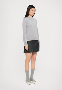 Grauer Strickpullover mit geripptem Kragen und Bündchen, kombiniert mit einem dunklen Jeansrock. Graue Socken und weiße spitze Schuhe runden den Look ab.
