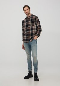 Camicia in flanella a quadri nei colori marrone, nero e panna, con taschino sul petto. Abbinata a jeans skinny blu scoloriti e stivali neri con lacci.