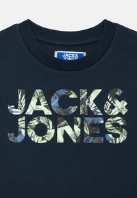 Temno mornarska majica s kapuco z napisom "JACK & JONES" v velikih, večbarvnih črkah z listnim vzorcem v zelenih in modrih odtenkih.