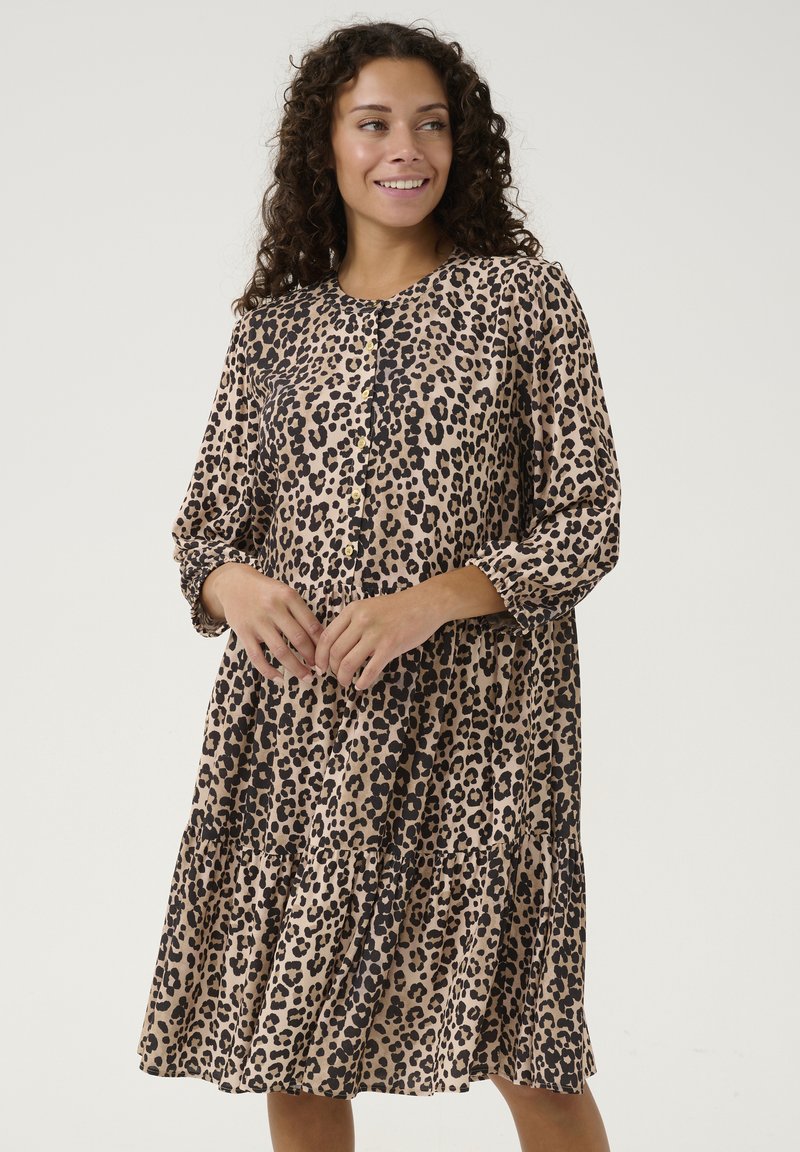 Rochie cu imprimeu leopard în nuanțe de bej și negru. Mâneci lungi, închidere cu nasturi și fustă plisată. Material fin cu o textură ușoară.