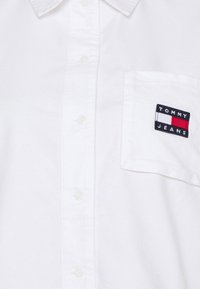 White button-up shirt made of cotton, featuring a left chest pocket with a multicolored "TOMMY JEANS" logo patch.