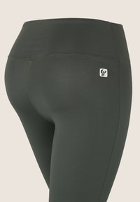 Leggings verde scuro realizzati in un tessuto liscio e stretch. Presentano una vita alta e cuciture a contrasto, con un piccolo emblema del logo sull'anca.