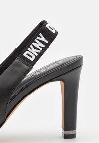 Sandale à talon noir avec un talon épais et une bride arrière élastique arborant la marque blanche "DKNY".