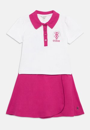 Polo blanco de manga corta con cuello y botones rosas, combinado con una falda rosa, con un pequeño logo bordado de GUESS en el pecho.