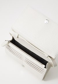 Cartera de cuero blanca con superficie texturizada, herrajes en plata, múltiples ranuras para tarjetas y un compartimento con cremallera. Interior forrado en negro.