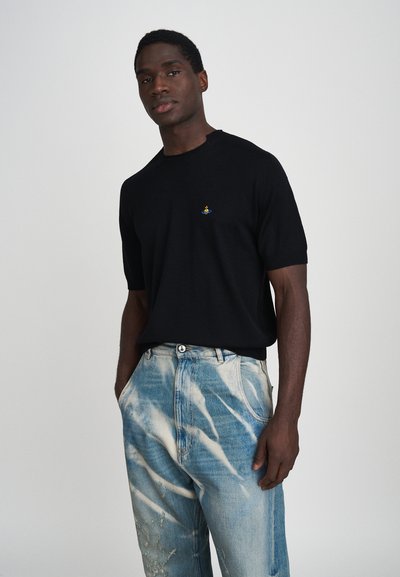 Zwarte kısa mouw gebreide t-shirt met een klein blauw en geel embleem op de borst, gecombineerd met lichtblauwe, versleten denim jeans.
