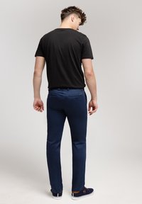 Czarna koszula z krótkim rękawem, zestawiona z dopasowanymi granatowymi spodniami i granatowymi butami z białymi podeszwami. Minimalistyczny design, gładka tekstura i dopasowany krój.