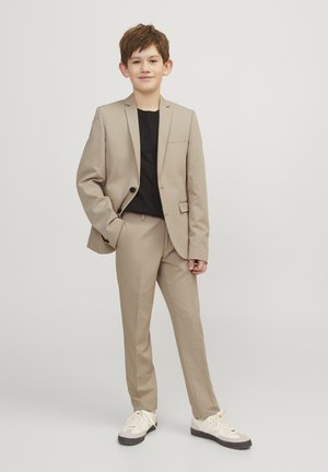 Beige sako s jedním knoflíkem, slim fit, s klopami; kombinováno s černým tričkem a teniskami. Hladká tkanina, módní střih.