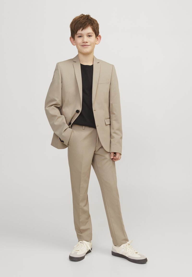 Beige kostym med enstaka knappstängning, slim fit, notched lapels; kombinerad med en svart t-shirt och sneakers. Slätt tyg, skräddarsydd design.