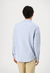 Camicia a maniche lunghe di colore azzurro chiaro realizzata in tessuto testurizzato. Presenta un orlo arrotondato e polsini con bottone, con un piccolo dettaglio di pettorale sul retro.