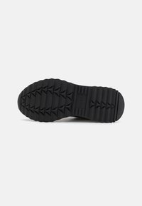 Semelle de chaussure en caoutchouc noir avec un motif de grip texturé. Présente des crans en relief en forme de triangle pour une traction et un design de talon plat.