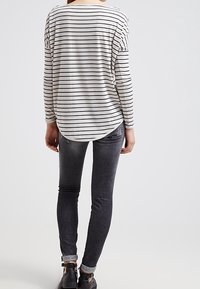 Gestreepte lange mouw top in lichtgrijs met zwarte strepen, gecombineerd met donkergrijze skinny jeans met een lichte wassing en opgerolde mouwen.