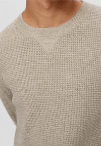 Maglione beige lavorato a maglia con un motivo texturizzato, caratterizzato da un collo rotondo e un piccolo dettaglio a forma di V nella zona del colletto.