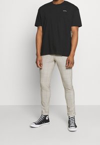 Svart bomullströja med en liten grafik, ljusbeige rutiga byxor och svarta högstövlar med vita sulor och svarta snören.