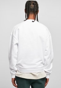 Hvid fleece sweatshirts med dolmanærmer og ribbede manchetter, med et enkelt design og blød tekstur, båret over et lysfarvet lag.