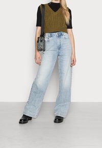 Woman wearing light blue wide-leg jeans, black short-sleeve top, olive green knit vest, black boots, and leopard print crossbody bag.