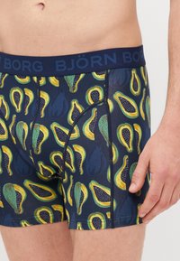 Navy blue boxer briefs with a colorful papaya fruit pattern. Elastic waistband features 'BJÖRN BORG' branding. Soft, stretchy fabric.