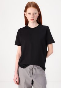 Sort kortærmet t-shirt lavet af solid bomuldsstof, med rund hals og en afslappet pasform. Kombineret med lysegrå bukser.