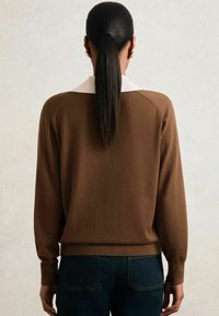 Pullover lavorato a maglia marrone con colletto bianco, maniche lunghe e vita a coste. Modello che indossa jeans blu scuro, visto di spalle.