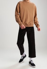 Brun crew neck sweatshirt, svarta kordflamsbyxor, vita strumpor och svarta skor. Avslappnad passform med ribbad mudd vid ärmar och midja.