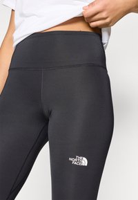 Μαύρο κολάν με λεία, ελαστική υφή. Διαθέτει φαρδύ ζωνάρι και λευκό λογότυπο της The North Face κοντά στο κάτω μέρος του ποδιού.