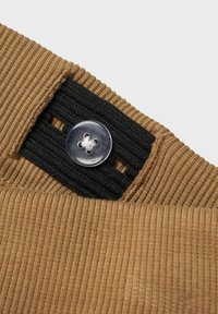 Pruun ribadega kangas musta elastse riba ja selge lillemustriga nupu detailiga. Close-up detail riideeseme kinnitamisest.