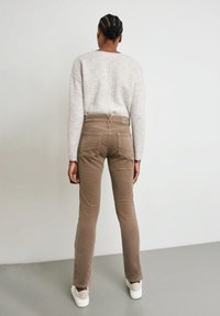 Pantalon en velours côtelé marron avec une coupe droite, doté de poches arrière et d'une petite étiquette de marque au niveau de la taille. Associé à un pull gris clair.
