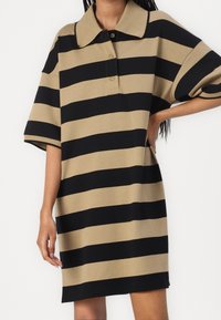 Pikétröja med kort ärm i svart och tan med växlande horisontella ränder; har en krage och en knappslå med tre knappar för stängning.