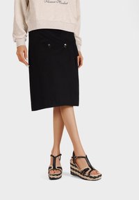 Gonna nera con due bottoni decorativi, abbinata a sandali con zeppa neri e beige a fantasia, dotati di design T-strap e fibbia regolabile.