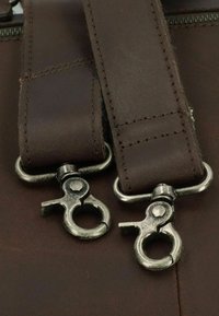 Correas de cuero marrón con clips de metal plateado, con detalles de costura. Los clips tienen un diseño de gancho para un ajuste seguro.