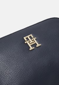 Granatowy skórzany portfel o fakturowanym wykończeniu. Charakteryzuje się wyraźnym złotym logo. Zbliżenie ukazujące detale materiału i designu.