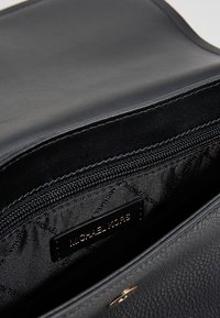Interno della borsa a tracolla in pelle nera che mostra una tasca con zip con etichetta "Michael Kors" su una fodera in tessuto nero.