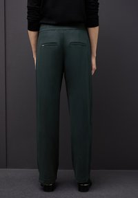 Pantalones de tejido verde y suave con un corte relajado, que cuentan con una cintura elástica y dos detalles de bolsillo en la parte posterior. Textura plana y corte recto.