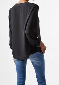 Blusa negra de manga larga con mangas abullonadas y acentos de botones, hecha de una tela suave. Usada con jeans ajustados azules.