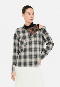 Schwarz-weißer Karobluse mit einem Spitzen-Einsatz, schulterfrei und langen Ärmeln. Verfügt über eine einzelne Brusttasche und eine Knopfleiste.