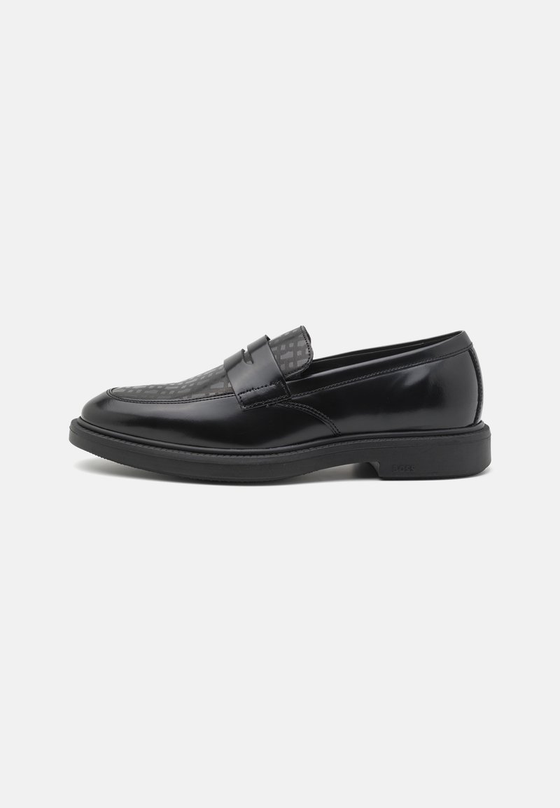 Mocassin en cuir noir poli, avec dessus à motifs et épaisse semelle noire, présenté de côté sur un fond clair uni.