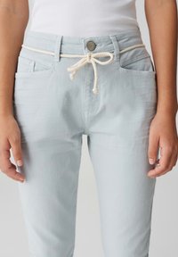 Pantalon bleu clair en tissu doux, doté d'une taille élastique avec un cordon de couleur crème, de poches avant et d'une fermeture à bouton.