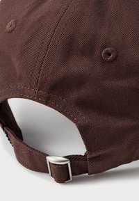 Brun bomullsmössa med en stuvad skärm och justerbar metallspänne i ryggen, med texturerad tyg och ventilationshål.