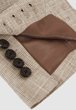 Material texturat de culoare bej cu un model în carouri. Interiorul are o căptușeală netedă de culoare maro. Patru nasturi întunecați sunt vizibili pe margine.