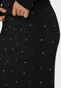 Falda de tela negra con una textura suave, que presenta detalles de cuentas blancas dispersas. La vista en primer plano muestra un sutil brillo y ajuste.