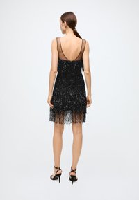 Black fringe dress with beaded texture, sleeveless design, V-back, and layered fringe hem. Matched with black high-heel sandals.
