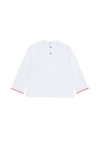 Camicia bianca a maniche lunghe con colletto arrotondato, cinque bottoni neri sul retro e rifinitura rosa a scallop sui polsini. Tessuto morbido.