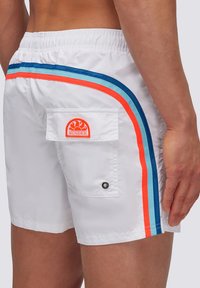 Pantaloni da bagno bianchi con elastico in vita, dotati di strisce laterali blu, arancioni e turchesi. Include una tasca posteriore con bottone a pressione e logo.