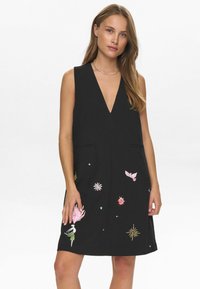 El vestido negro sin mangas presenta un escote en V profundo, dos bolsillos y vibrantes diseños bordados de flores y estrellas en rosa, dorado y azul.
