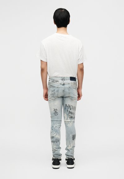 Helesinis kulunud teksapüksid, millel on mitmesugused mustad graffitistiilis trükised, viis taskut ja seljal kantud tavaline valge t-särk.