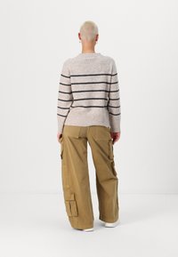 Beige striped sweater with a ribbed hem paired with loose khaki cargo pants featuring large pockets and a relaxed fit. White shoes visible.