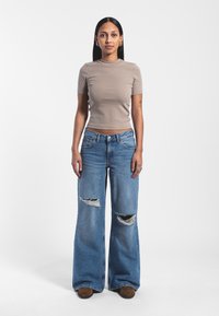 T-shirt beige aderente a maniche corte abbinato a jeans a gamba larga blu chiaro con strappi sulla parte anteriore. Le calzature consistono in mocassini marroni.