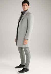 Abrigo de lana gris claro con un diseño estructurado y solapas con muesca, combinado con pantalones gris ajustados y zapatillas negras. Textura suave, corte a medida.