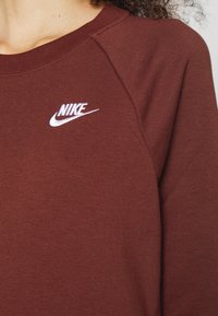 Sweatshirt bordeaux avec un col rond côtelé. Présente un logo Nike brodé en blanc sur la poitrine gauche. Fabriqué à partir d'un tissu texturé doux.