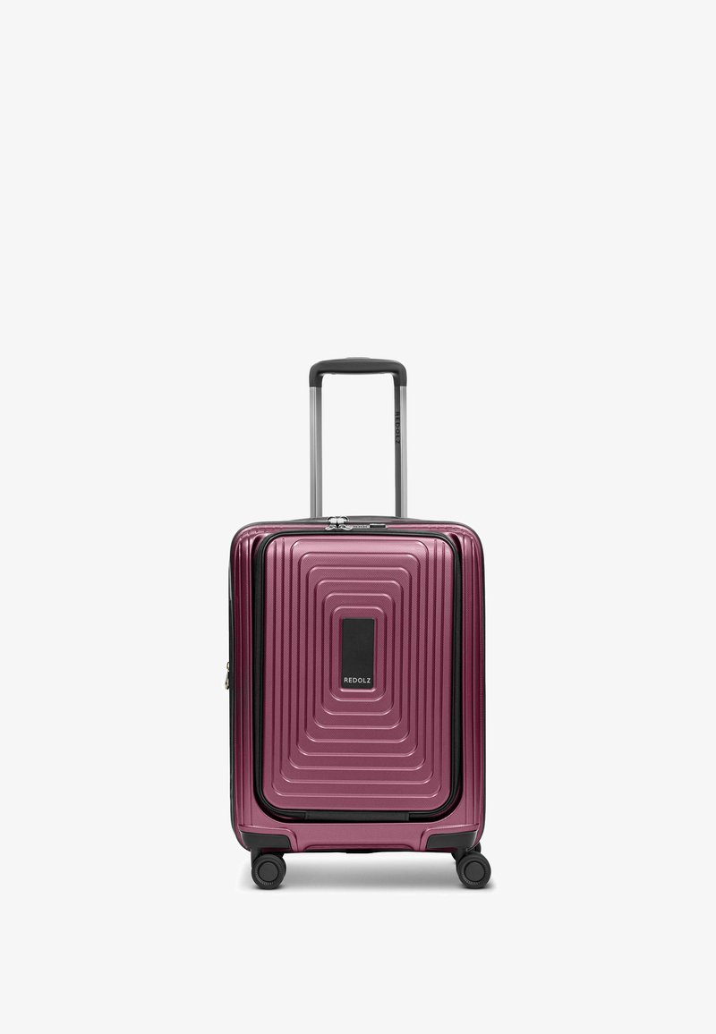 Valigia rigida viola con un design a linee concentriche testurizzate, doppie ruote nere, manico retrattile e un pannello centrale con logo.